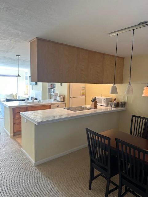 kitchen featuring kitchen peninsula, a kitchen bar, sink, white appliances, and hanging light fixtures