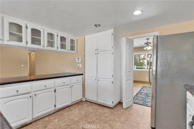 kitchen featuring stainless steel fridge, dark stone countertops, white cabinetry, a textured ceiling, and ceiling fan