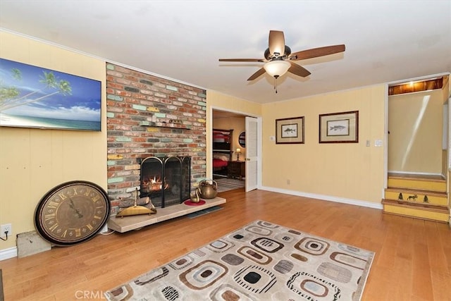 living room with hardwood / wood-style flooring, ceiling fan, ornamental molding, and a fireplace