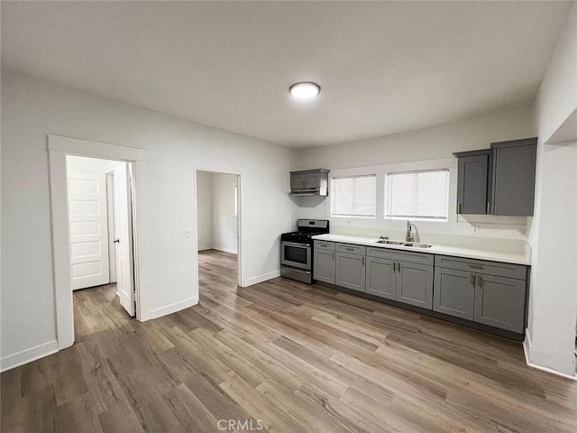 kitchen featuring light wood-style floors, light countertops, gray cabinetry, stainless steel range oven, and a sink