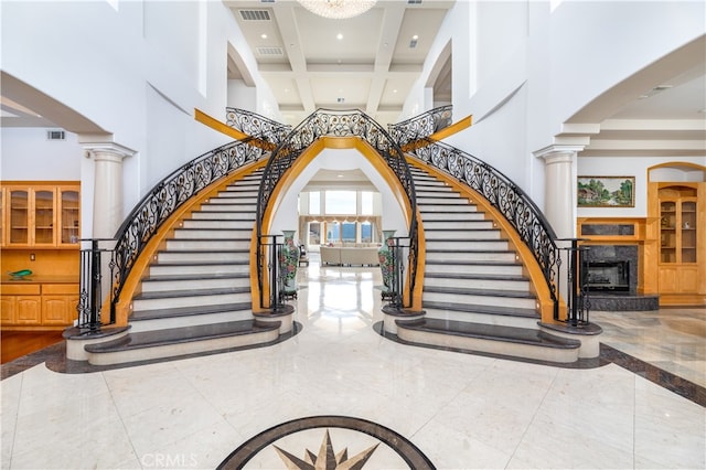 stairs featuring beamed ceiling, a high end fireplace, decorative columns, and a high ceiling