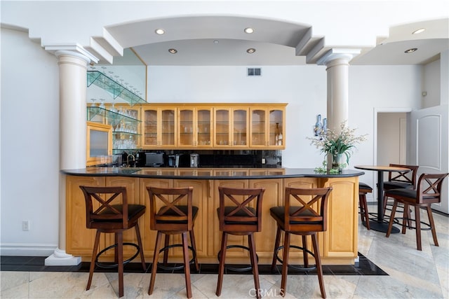 bar with decorative columns, decorative backsplash, and light tile patterned floors