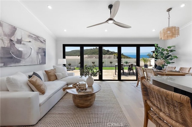 living room featuring ornamental molding, a water view, ceiling fan, and light wood-type flooring