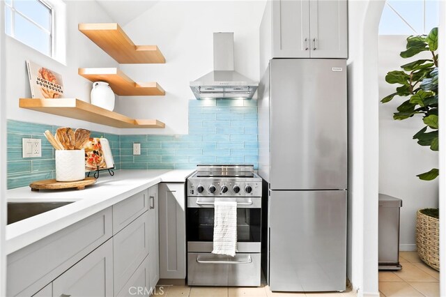 kitchen with wall chimney range hood, decorative backsplash, light tile patterned floors, and appliances with stainless steel finishes