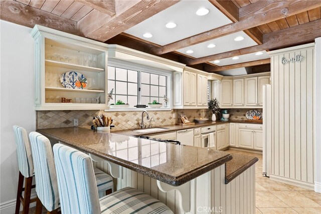 kitchen featuring sink, a kitchen breakfast bar, kitchen peninsula, beamed ceiling, and dark stone counters