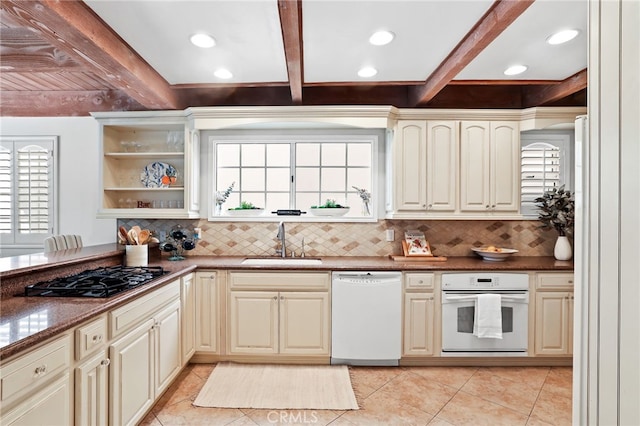 kitchen with beamed ceiling, sink, white appliances, and dark stone counters