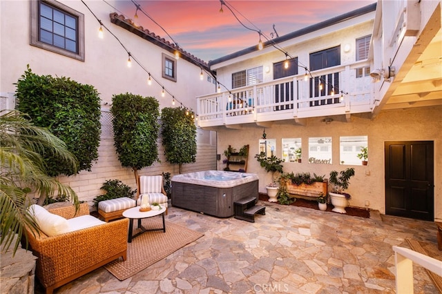 patio terrace at dusk with a hot tub and a balcony