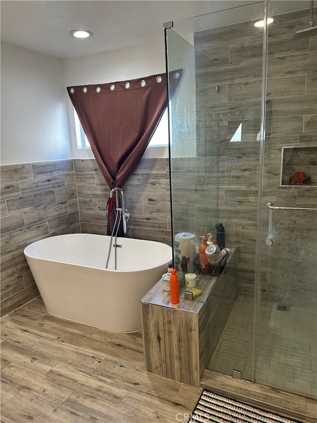 bathroom with plus walk in shower, hardwood / wood-style floors, and tile walls