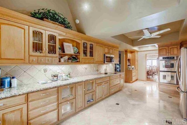 kitchen with lofted ceiling, light stone counters, ceiling fan, stainless steel appliances, and backsplash