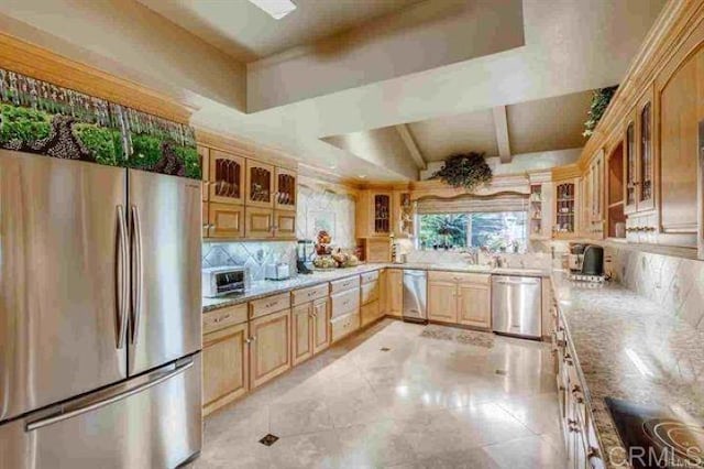 kitchen with light brown cabinets, vaulted ceiling, light stone counters, stainless steel appliances, and backsplash