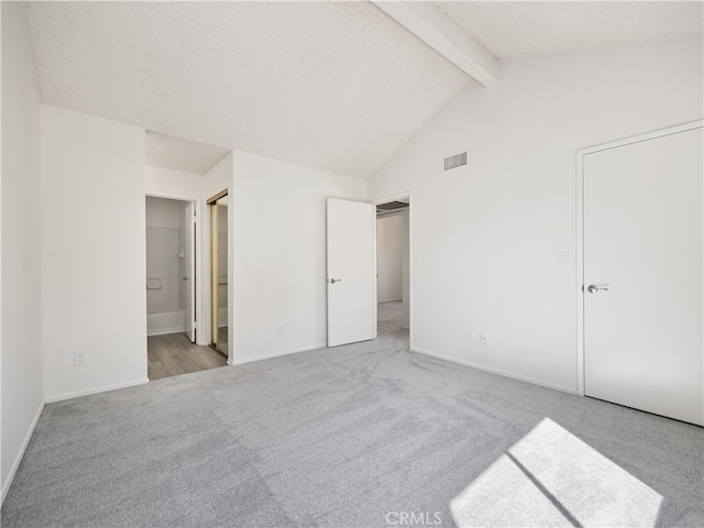 unfurnished bedroom with connected bathroom, a textured ceiling, light carpet, and vaulted ceiling with beams