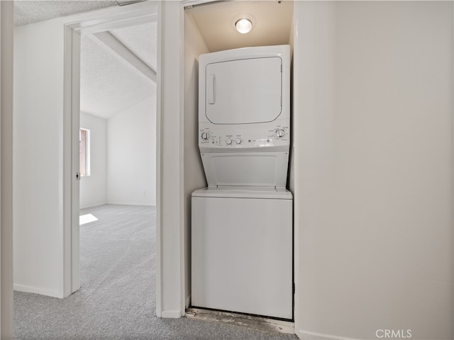 washroom featuring stacked washer / drying machine, light colored carpet, and a textured ceiling