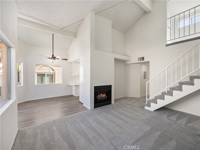 unfurnished living room with high vaulted ceiling, a textured ceiling, ceiling fan, beam ceiling, and carpet