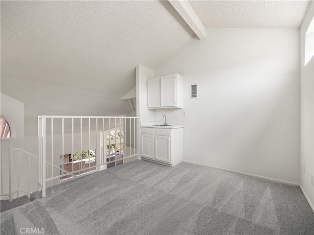 carpeted empty room with sink, a textured ceiling, vaulted ceiling with beams, and a healthy amount of sunlight