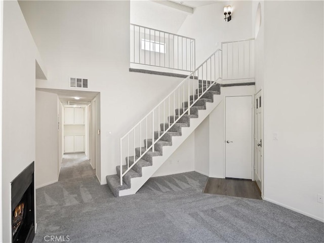 stairway with beamed ceiling, carpet floors, and a high ceiling