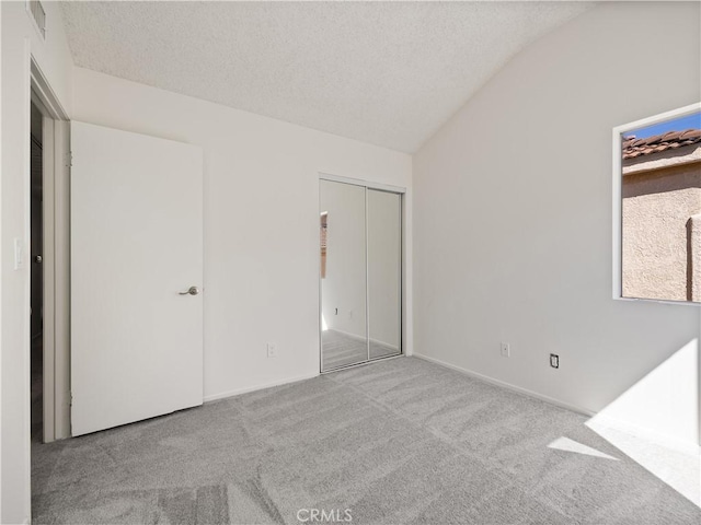 unfurnished bedroom with lofted ceiling, light carpet, a textured ceiling, and a closet