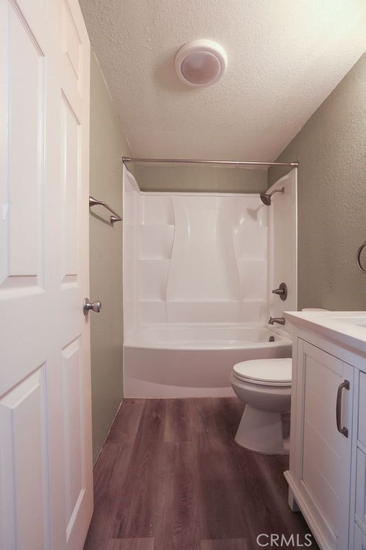 full bathroom with vanity, toilet, a textured ceiling, wood-type flooring, and tub / shower combination