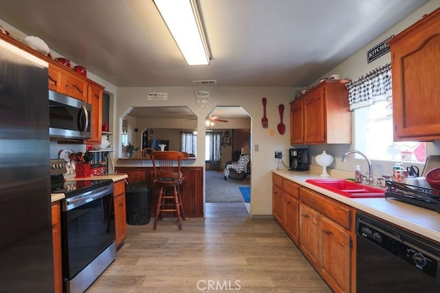 kitchen with light wood-type flooring, stainless steel appliances, ceiling fan, sink, and a breakfast bar area