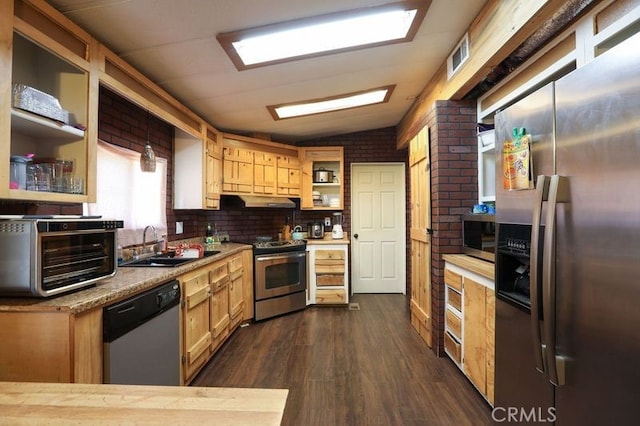 kitchen with appliances with stainless steel finishes, brick wall, vaulted ceiling, dark hardwood / wood-style floors, and hanging light fixtures