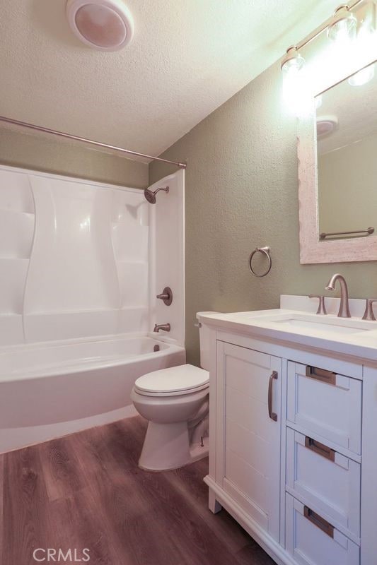 full bathroom with vanity, a textured ceiling,  shower combination, hardwood / wood-style flooring, and toilet