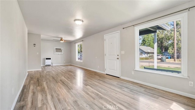 unfurnished room featuring ceiling fan, light hardwood / wood-style flooring, heating unit, and a wall mounted air conditioner