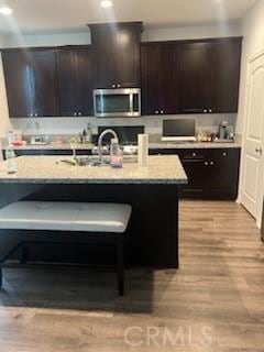 kitchen with light stone countertops, dark brown cabinets, range, light hardwood / wood-style floors, and an island with sink