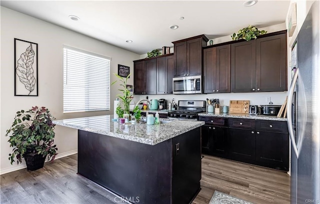 kitchen with a center island with sink, stainless steel appliances, dark brown cabinets, and wood-type flooring