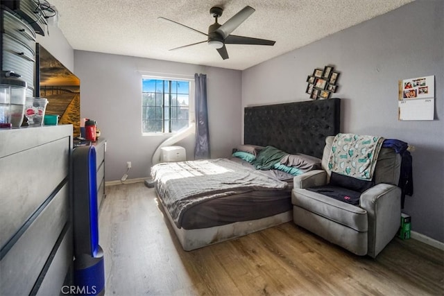 bedroom with a ceiling fan, a textured ceiling, baseboards, and wood finished floors