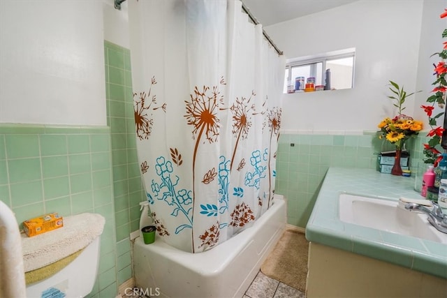 bathroom with wainscoting, tile patterned floors, shower / bath combo with shower curtain, vanity, and tile walls