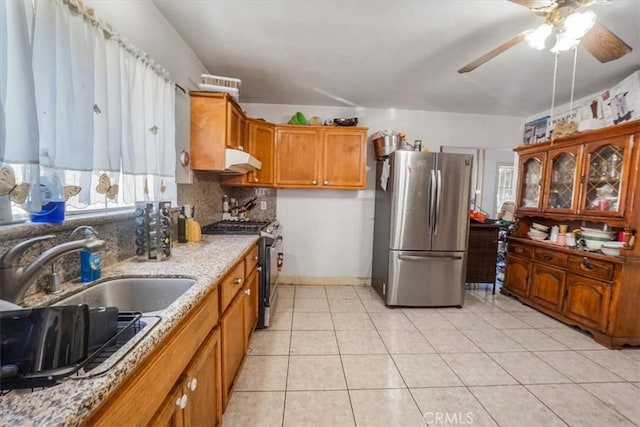 kitchen featuring light tile patterned floors, light stone counters, brown cabinets, stainless steel appliances, and under cabinet range hood