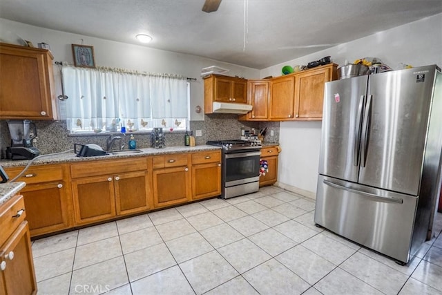 kitchen with brown cabinets, appliances with stainless steel finishes, a sink, light stone countertops, and under cabinet range hood