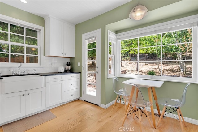 kitchen with white cabinets, a healthy amount of sunlight, light wood-type flooring, and tasteful backsplash