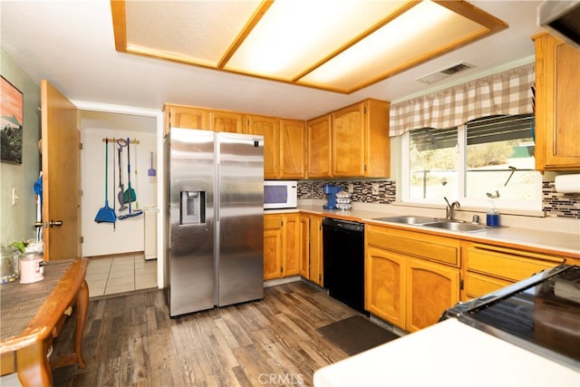 kitchen featuring black dishwasher, stainless steel fridge, sink, backsplash, and wood-type flooring