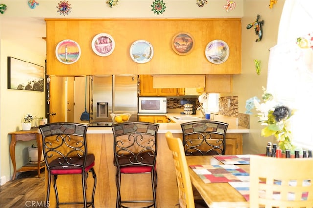 kitchen with stainless steel refrigerator with ice dispenser, hardwood / wood-style floors, sink, a breakfast bar, and kitchen peninsula