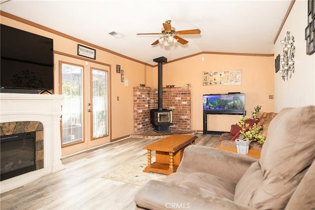 living room with a wood stove, crown molding, ceiling fan, hardwood / wood-style flooring, and vaulted ceiling