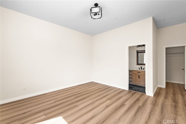 unfurnished bedroom featuring light wood-type flooring, ensuite bath, and sink