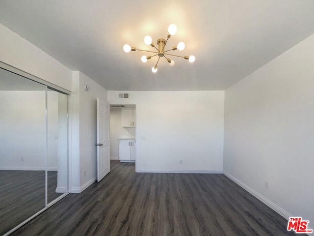 unfurnished bedroom featuring a notable chandelier, a closet, and dark wood-type flooring