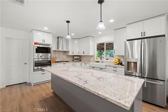 kitchen featuring a center island, white cabinetry, wall chimney exhaust hood, appliances with stainless steel finishes, and decorative light fixtures