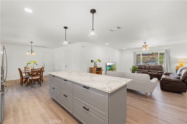 kitchen featuring light hardwood / wood-style floors, light stone countertops, gray cabinets, a center island, and decorative light fixtures