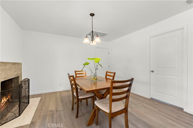 dining area with a fireplace, light hardwood / wood-style flooring, and a notable chandelier