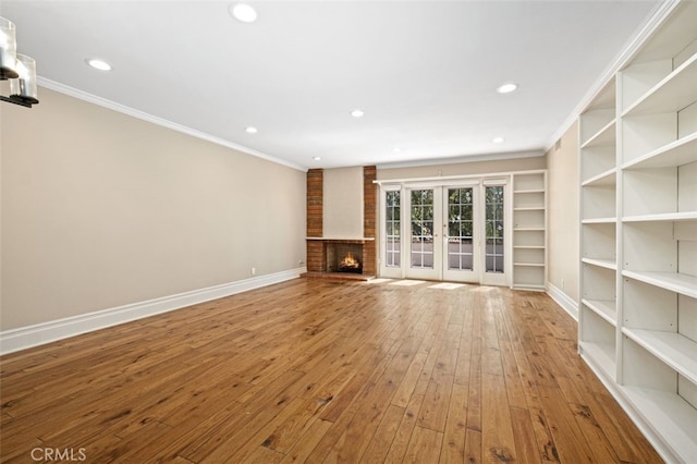 unfurnished living room featuring hardwood / wood-style floors, a fireplace, french doors, and crown molding