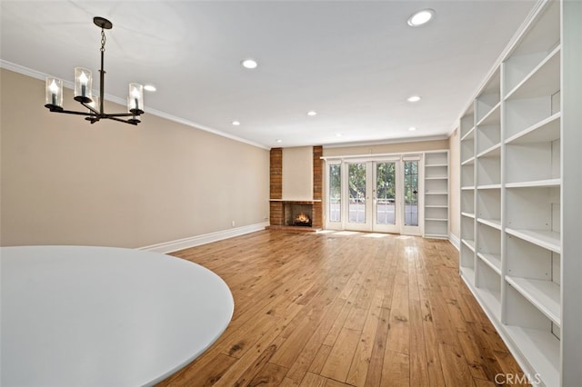 unfurnished living room featuring ornamental molding, a brick fireplace, a chandelier, and hardwood / wood-style floors