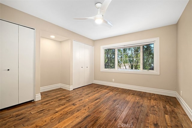 unfurnished bedroom with ceiling fan, two closets, and dark hardwood / wood-style floors