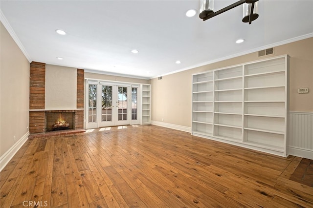 unfurnished living room with wood-type flooring, a fireplace, crown molding, and french doors