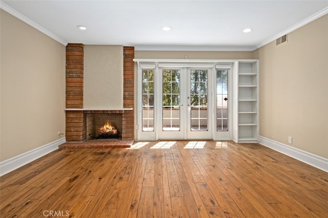 unfurnished living room featuring a fireplace, hardwood / wood-style flooring, french doors, and crown molding