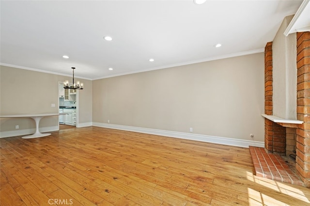 unfurnished living room with a brick fireplace, a notable chandelier, light wood-type flooring, and ornamental molding