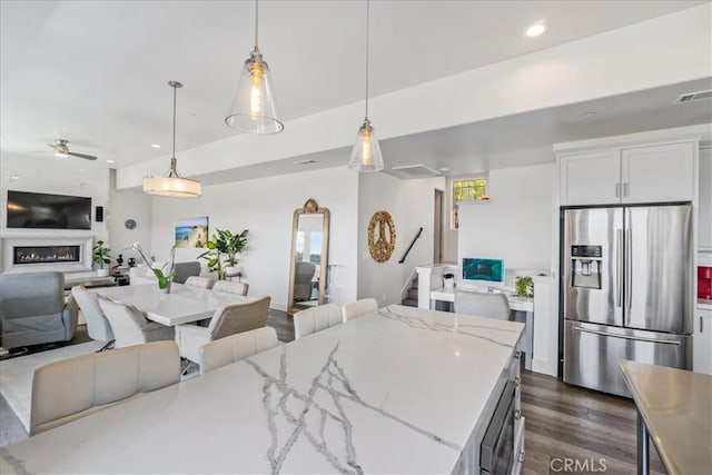 kitchen featuring light stone countertops, white cabinetry, dark hardwood / wood-style floors, stainless steel refrigerator with ice dispenser, and pendant lighting