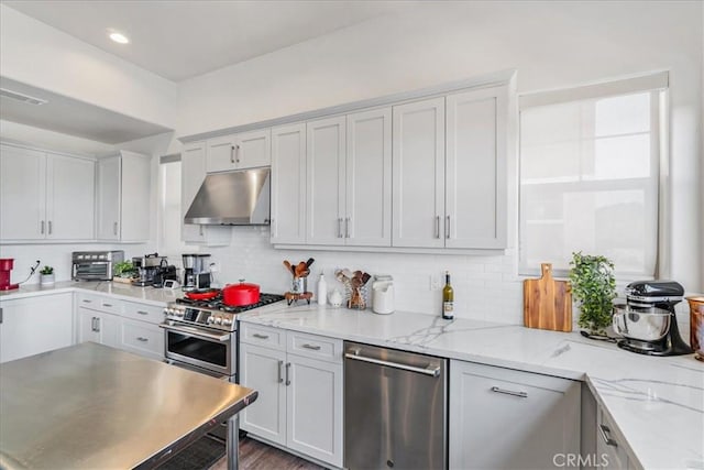 kitchen featuring dark wood-type flooring, exhaust hood, decorative backsplash, light stone counters, and stainless steel appliances