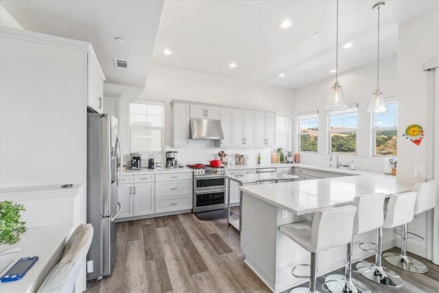 kitchen with a kitchen breakfast bar, stainless steel appliances, white cabinets, light hardwood / wood-style floors, and hanging light fixtures