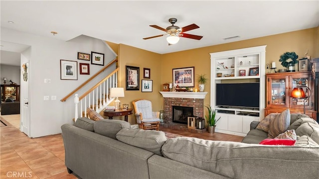 living area featuring built in shelves, a fireplace, light tile patterned floors, a ceiling fan, and stairs